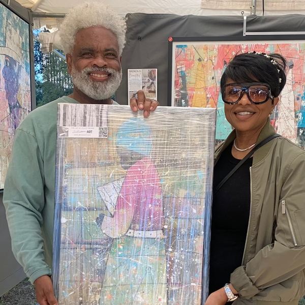 An older man and a woman standing outdoors under a tent, holding up a large, wrapped canvas painting. The painting features an abstract colorful design with a figure in a pink dress.